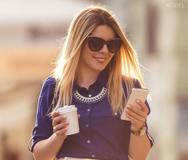 Model holding cup of coffee looking at phone