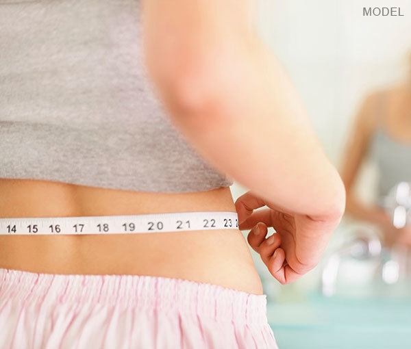 Model measuring her waste with a tape measure