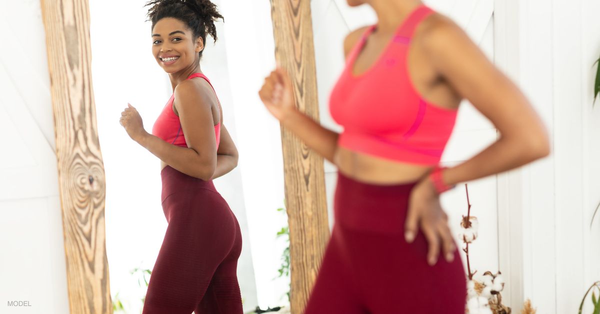 Woman with an athletic figure (model) looking at herself in the mirror and smiling.