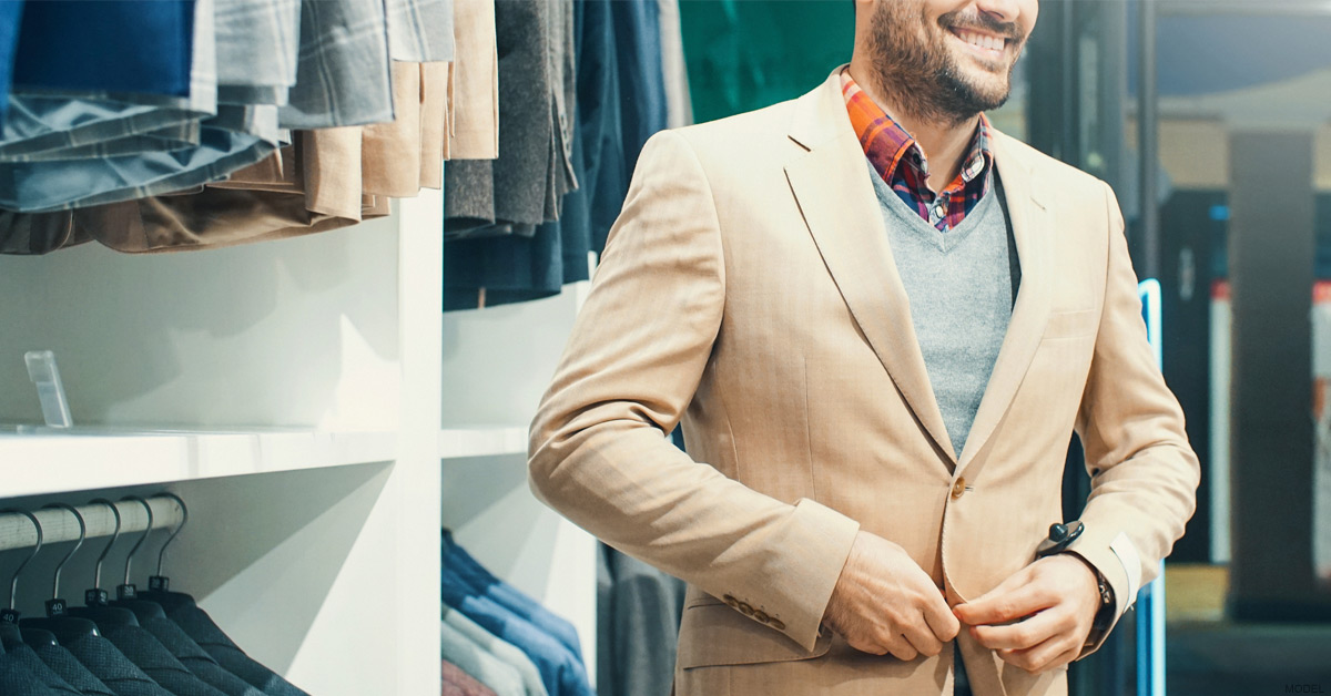 Man adjusting his beige suit jacket while shopping in a clothing store.